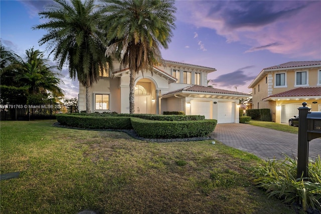 mediterranean / spanish-style home featuring an attached garage, driveway, a front lawn, and stucco siding