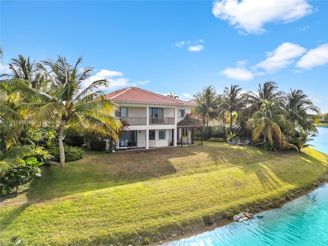 rear view of property featuring a water view, stucco siding, a yard, and a balcony