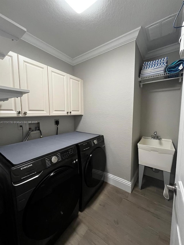 laundry room with cabinet space, light wood finished floors, visible vents, ornamental molding, and washer and clothes dryer