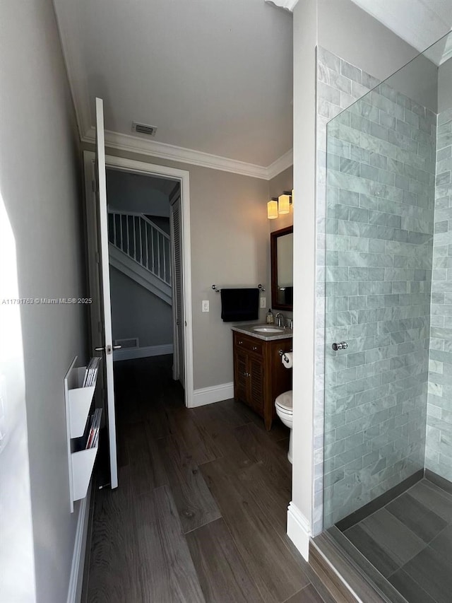 full bath featuring visible vents, a tile shower, wood finished floors, vanity, and ornamental molding