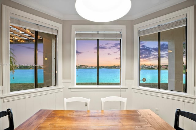 dining space featuring crown molding, a water view, a healthy amount of sunlight, and a decorative wall