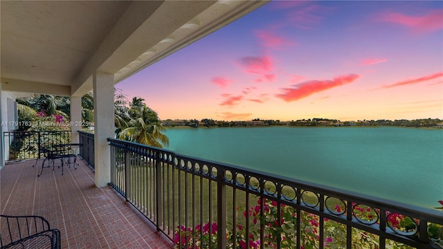 balcony at dusk featuring a water view