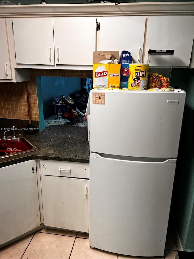 kitchen with backsplash, a sink, light tile patterned floors, freestanding refrigerator, and white cabinetry