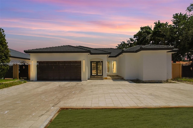 view of front of property featuring a tile roof, decorative driveway, fence, an attached garage, and stucco siding