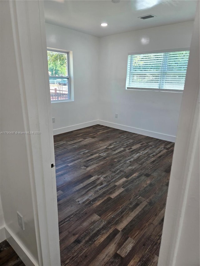 empty room featuring baseboards, visible vents, and dark wood-style floors