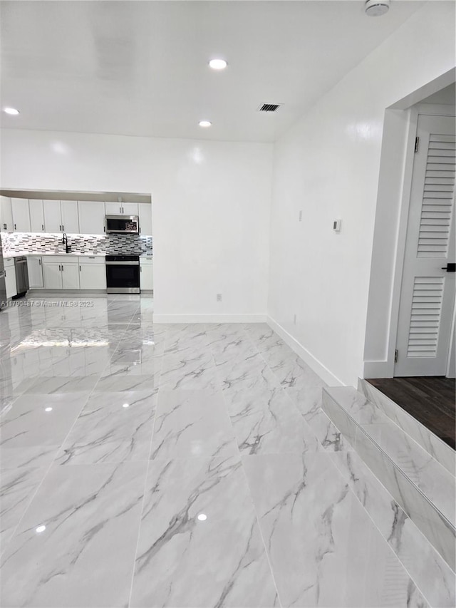 unfurnished living room featuring visible vents, a sink, baseboards, and recessed lighting