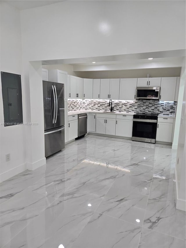 kitchen featuring electric panel, appliances with stainless steel finishes, tasteful backsplash, a sink, and baseboards