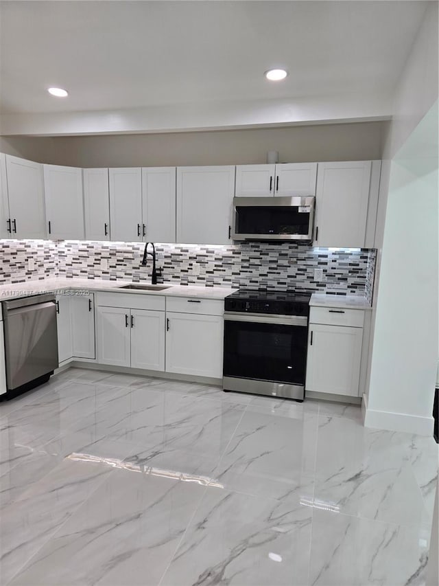 kitchen with backsplash, a sink, white cabinets, stainless steel appliances, and recessed lighting