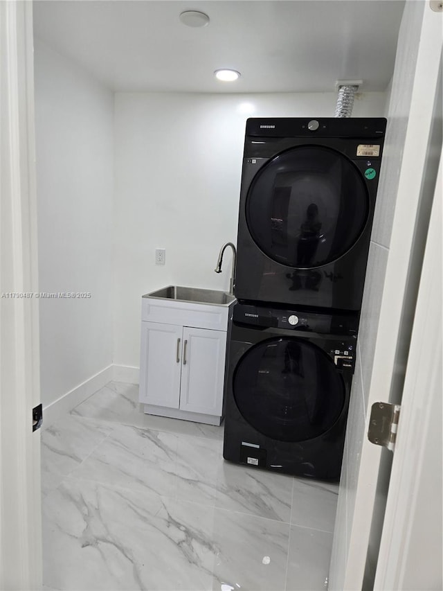 laundry room featuring cabinet space, stacked washer and dryer, a sink, marble finish floor, and baseboards
