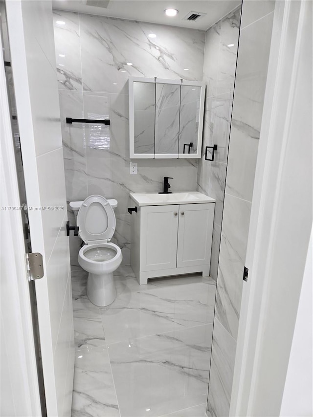 bathroom featuring tile walls, visible vents, toilet, and marble finish floor