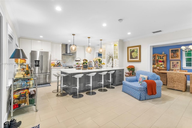 kitchen with wall chimney range hood, a kitchen breakfast bar, visible vents, light countertops, and high end fridge