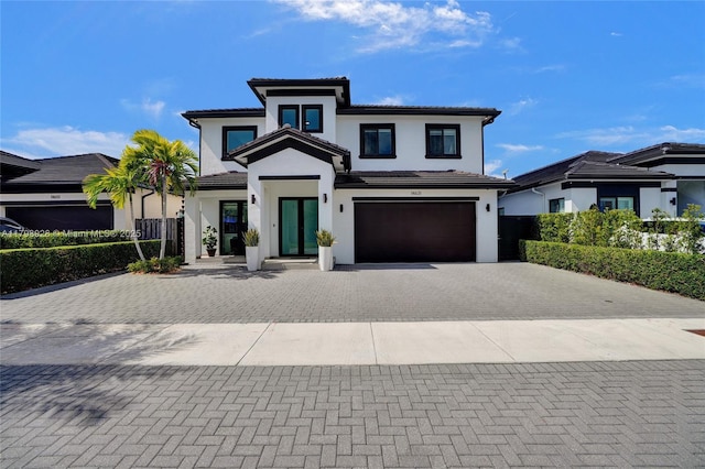 view of front of home featuring stucco siding, an attached garage, a tile roof, and decorative driveway