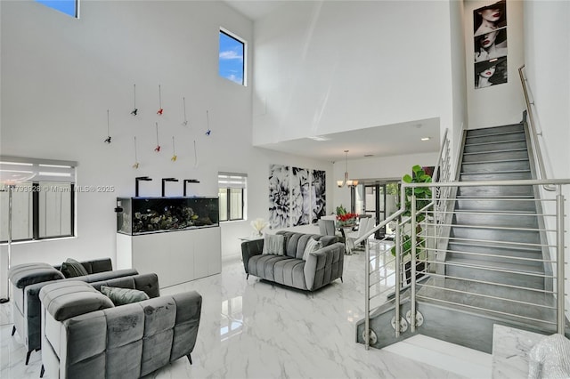 living area featuring a towering ceiling, plenty of natural light, stairs, and marble finish floor