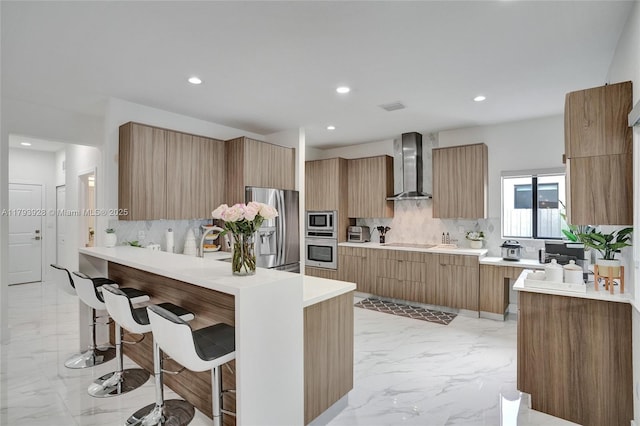 kitchen featuring marble finish floor, modern cabinets, a kitchen bar, wall chimney exhaust hood, and stainless steel appliances