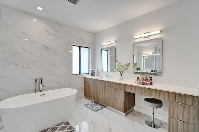 full bathroom featuring vanity, marble finish floor, a freestanding bath, and visible vents
