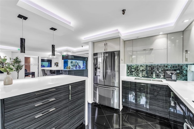 kitchen featuring modern cabinets, light countertops, stainless steel fridge with ice dispenser, a sink, and decorative light fixtures