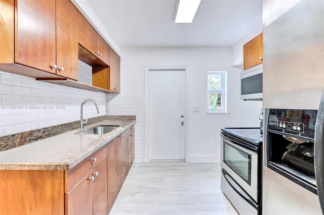 kitchen featuring a sink, brown cabinetry, stainless steel appliances, and light wood-style flooring