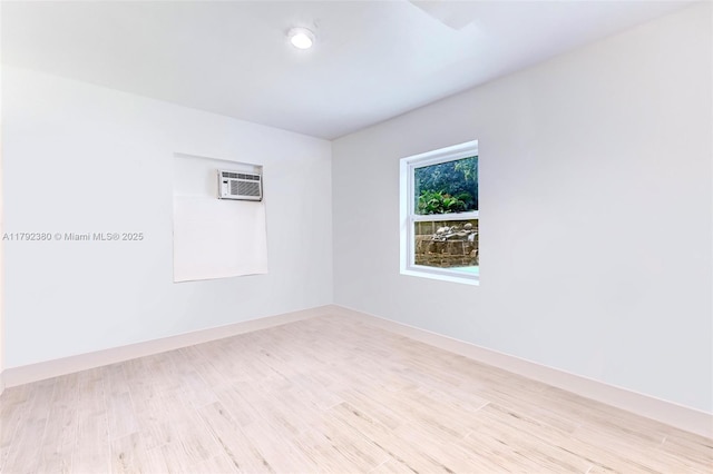 empty room with baseboards, an AC wall unit, and light wood finished floors