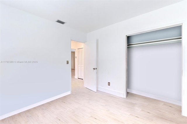 unfurnished bedroom with visible vents, light wood-style floors, baseboards, and a closet
