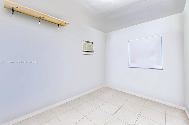 unfurnished room with an AC wall unit, baseboards, and light tile patterned floors