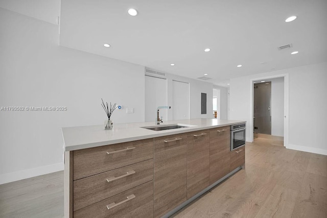650 NE 32nd St Unit 1004, Miami, FL 33137 - kitchen with modern cabinets, a center island with sink, a sink, stainless steel oven, and light wood-style flooring