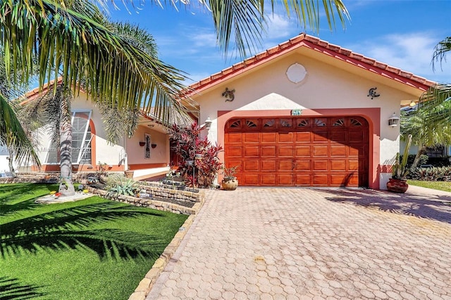 mediterranean / spanish-style home with a front yard, decorative driveway, stucco siding, a tiled roof, and an attached garage
