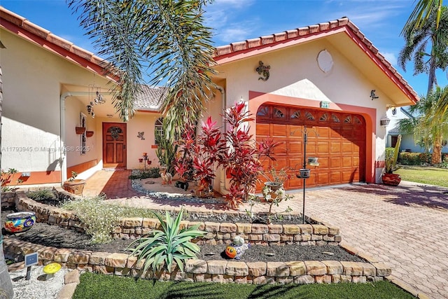 mediterranean / spanish house with an attached garage, decorative driveway, stucco siding, and a tile roof