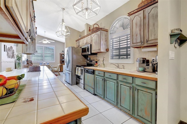 kitchen with light tile patterned flooring, a sink, stainless steel appliances, tile countertops, and lofted ceiling