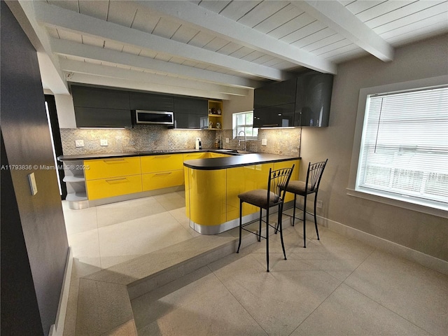 kitchen with open shelves, dark countertops, a peninsula, stainless steel microwave, and backsplash
