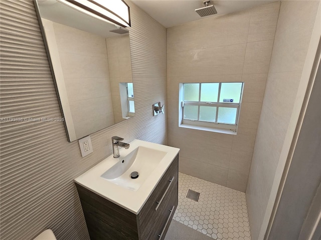 bathroom featuring visible vents, tile walls, tile patterned flooring, a tile shower, and vanity