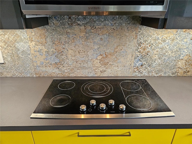 interior details with decorative backsplash, under cabinet range hood, black electric stovetop, and dark countertops