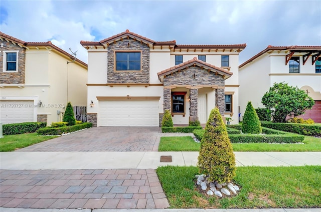mediterranean / spanish house with decorative driveway, a garage, stone siding, and stucco siding