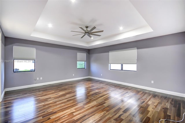 empty room with ceiling fan, dark wood finished floors, baseboards, and a raised ceiling