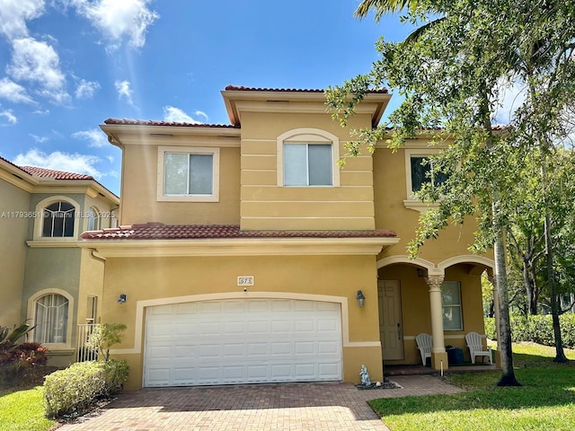 mediterranean / spanish home featuring a tiled roof, decorative driveway, an attached garage, and stucco siding