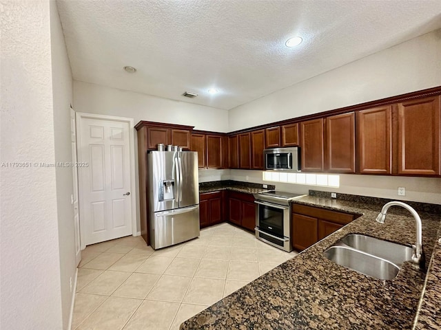 kitchen with a sink, light tile patterned floors, stainless steel appliances, and a textured ceiling