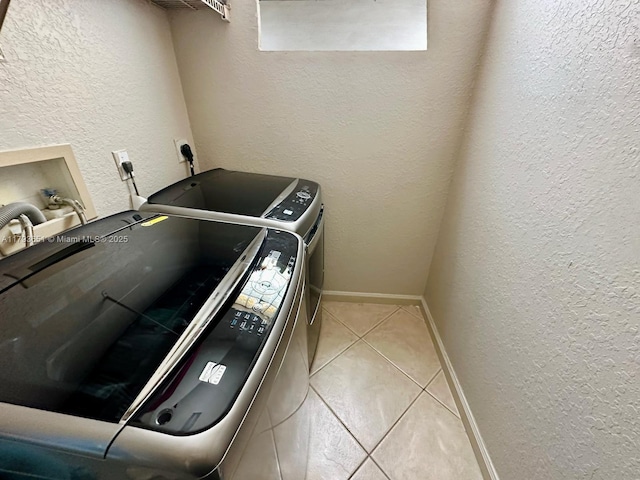 laundry area featuring separate washer and dryer, laundry area, a textured wall, and light tile patterned floors