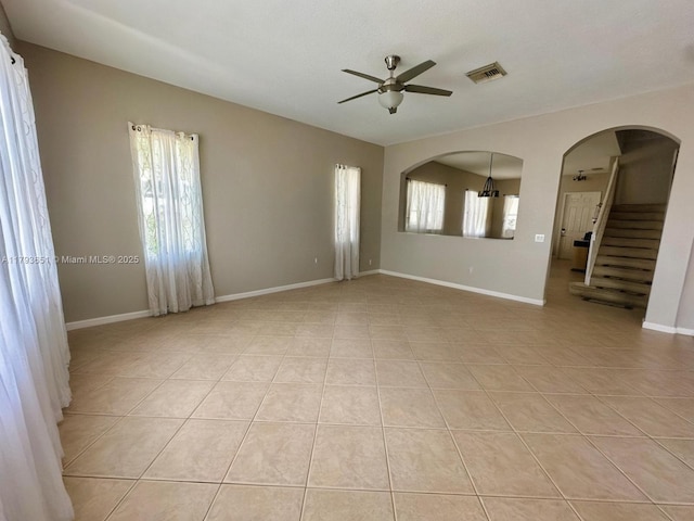 empty room with ceiling fan, visible vents, arched walkways, light tile patterned floors, and stairs