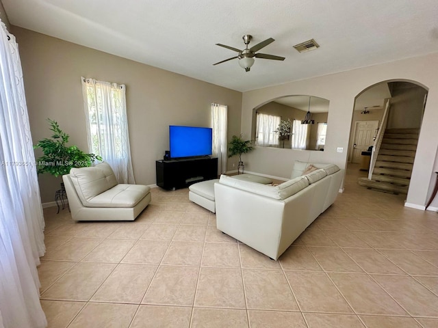 living room with arched walkways, a ceiling fan, light tile patterned floors, visible vents, and stairway