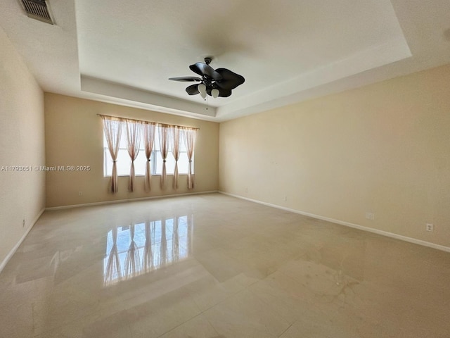 spare room with baseboards, a ceiling fan, a tray ceiling, and visible vents