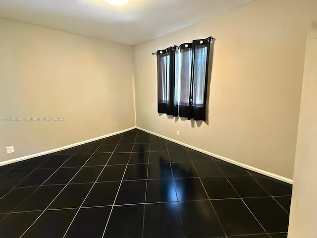 unfurnished room with dark tile patterned floors and baseboards