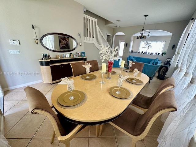 dining room featuring baseboards, arched walkways, stairs, and light tile patterned floors