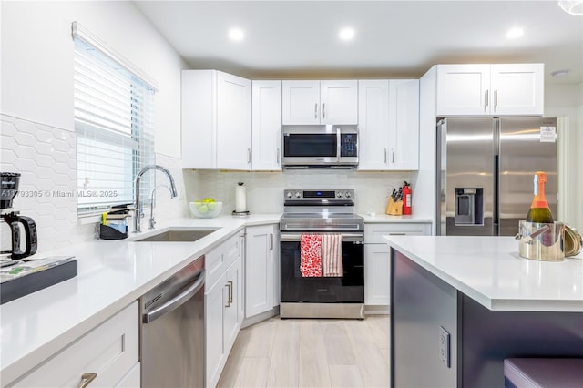 kitchen featuring appliances with stainless steel finishes, tasteful backsplash, a sink, light countertops, and white cabinetry