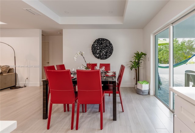 dining space featuring baseboards, a tray ceiling, light wood finished floors, and visible vents
