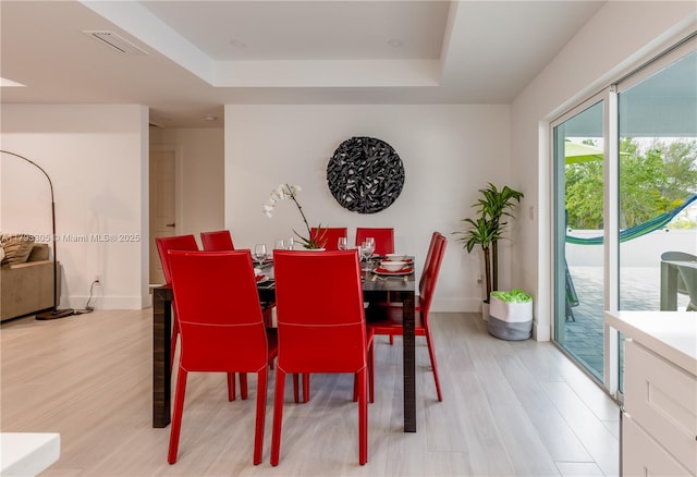 dining area featuring a raised ceiling, baseboards, light wood-style flooring, and visible vents