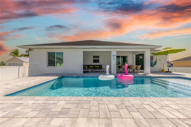 back of house at dusk featuring fence, an outdoor pool, a patio area, and stucco siding