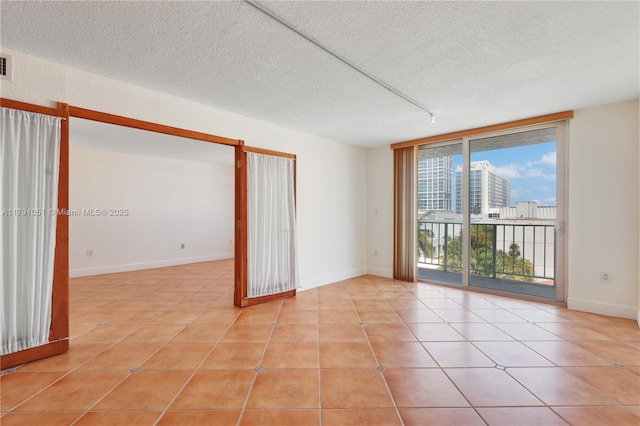 spare room featuring a wall of windows, light tile patterned flooring, rail lighting, and a textured ceiling