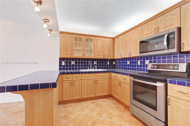 kitchen featuring light brown cabinetry, stainless steel appliances, tile countertops, and a sink
