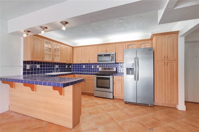 kitchen with light brown cabinets, a breakfast bar, glass insert cabinets, tile countertops, and appliances with stainless steel finishes