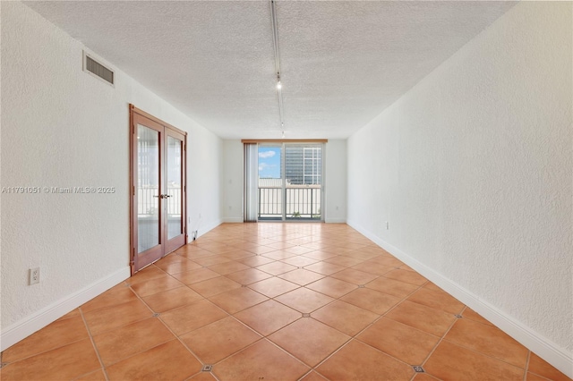 spare room featuring a textured ceiling, visible vents, a textured wall, and light tile patterned floors