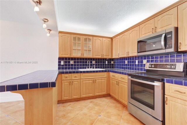 6801 Indian Creek Dr Unit 602, Miami Beach, FL 33141 - kitchen featuring appliances with stainless steel finishes, tile counters, light brown cabinetry, a sink, and a textured ceiling